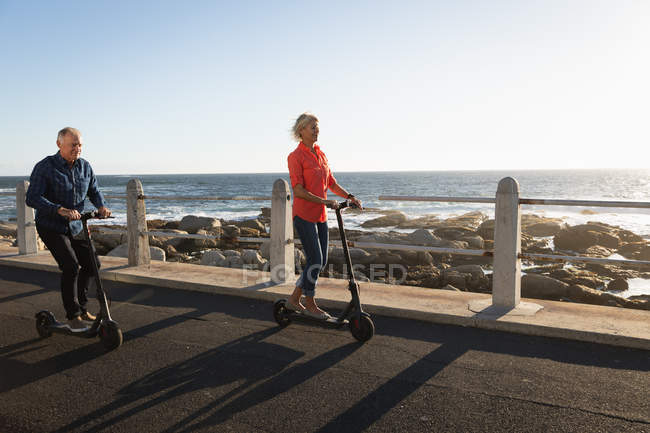 Front view close up of a mature Caucasian man and woman riding e scooters by the sea at sunset — Stock Photo
