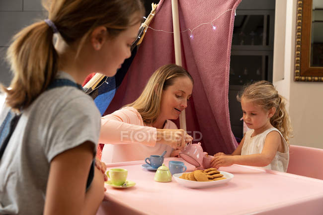Side view of a young Caucasian woman with her tween and younger daughters having a dolls tea party at home — стокове фото