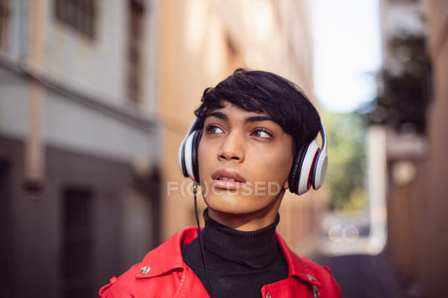 Vue de face d'un jeune transgenre mixte à la mode adulte dans la rue, avec écouteurs allumés — Photo de stock