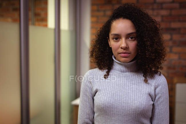 Porträt einer jungen Frau mit gemischter Rasse, die im Büro eines kreativen Unternehmens arbeitet und direkt in die Kamera blickt — Stockfoto