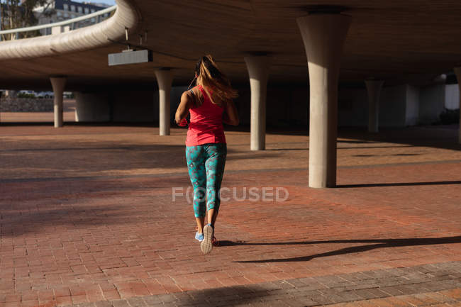 Vista posteriore di una giovane donna caucasica che indossa abiti sportivi in esecuzione durante un allenamento in una giornata di sole in un parco — Foto stock