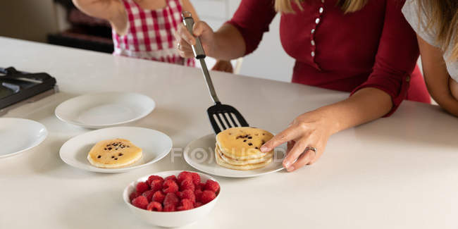 Front view close up of woman making pancakes in the kitchen at home with her tween and younger daughters — Stock Photo