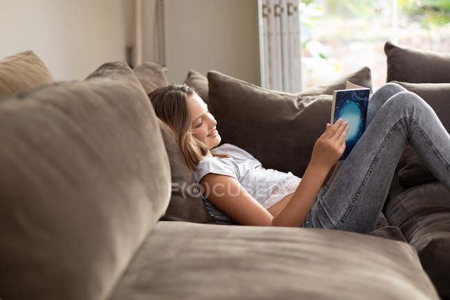 Вид сбоку на юную кавказскую девушку, читающую в гостиной — стоковое фото