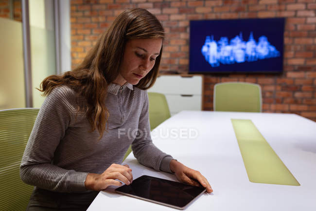 Зворотний бік зображення молодої кавказької жінки, яка працює в офісі творчого бізнесу сидячи за столом за планшетним комп'ютером. — стокове фото