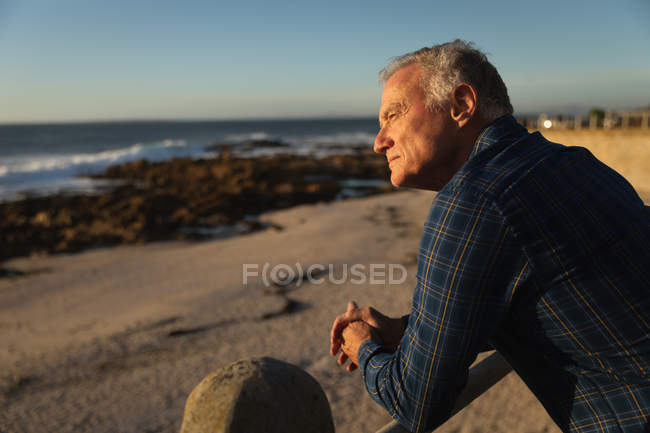Vista lateral de perto de um homem caucasiano maduro admirando a vista pelo mar ao pôr do sol — Fotografia de Stock