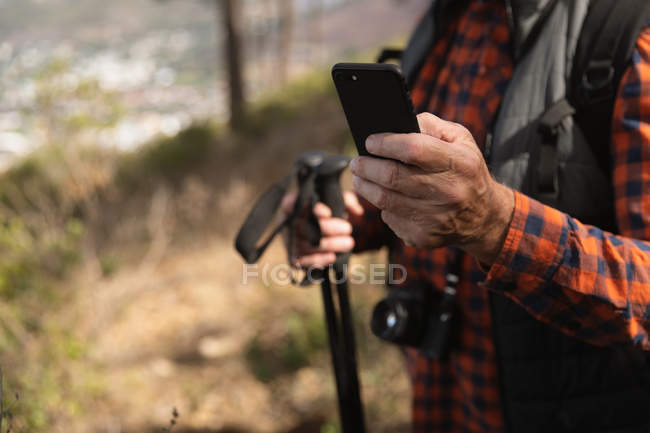 Вид на середину чоловіка за допомогою смартфона і тримають скандинавські палички для ходьби в сільській місцевості. — стокове фото