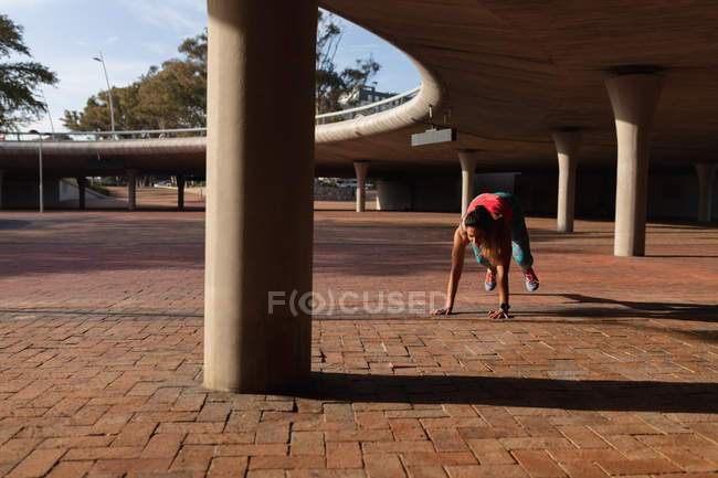 Front view of a young Caucasian woman wearing sports clothes doing burpees during a workout on a sunny day in a park — Stock Photo