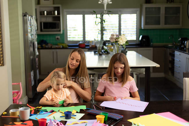 Vorderansicht einer jungen kaukasischen Frau, die mit ihren Zwillingen und jüngeren Töchtern im Wohnzimmer bastelt — Stockfoto