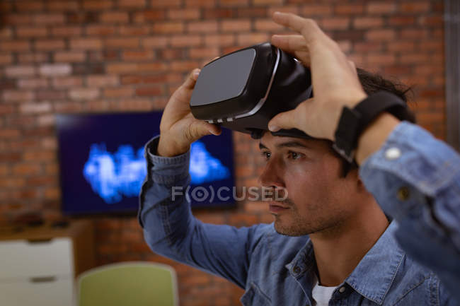 Vue de côté gros plan d'un jeune homme caucasien assis à un bureau portant un casque VR dans le bureau d'une entreprise créative — Photo de stock