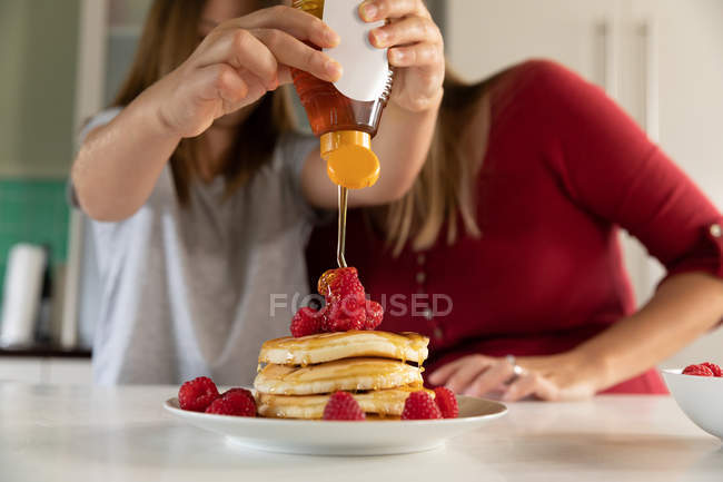 Vorderansicht einer jungen kaukasischen Frau, die in der Küche zu Hause mit ihren Zwillingen Pfannkuchen backt — Stockfoto