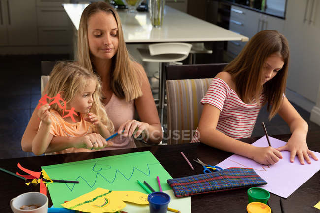 Vista frontal de una joven mujer caucásica haciendo manualidades con sus hijas adolescentes y más jóvenes en su sala de estar - foto de stock