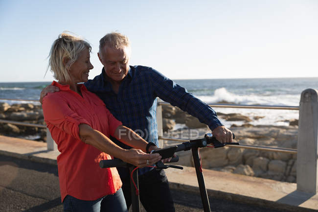 Front view of a mature Caucasian man and woman taking a selfie on e scooters by the sea — Stock Photo
