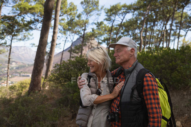 Vista lateral de um homem e mulher caucasiano maduro abraçando durante uma caminhada em um ambiente rural — Fotografia de Stock