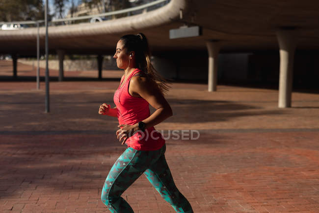 Vue de côté gros plan d'une jeune femme caucasienne portant des vêtements de sport courant pendant une séance d'entraînement par une journée ensoleillée dans un parc — Photo de stock