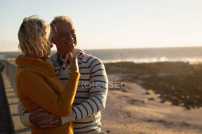 Vista frontal de cerca de un hombre y una mujer caucásicos maduros abrazándose por el mar al atardecer - foto de stock