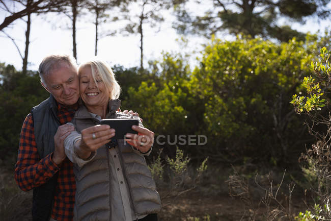 Vista frontal de un hombre y una mujer caucásicos sonrientes y maduros tomando una selfie juntos durante un paseo por el campo - foto de stock