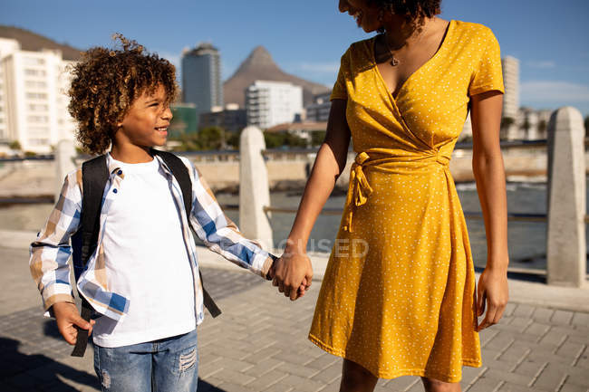 Front view of a young mixed race woman and her pre-teen son enjoying time together by the sea, holding hands and walking on a sunny day — Stock Photo