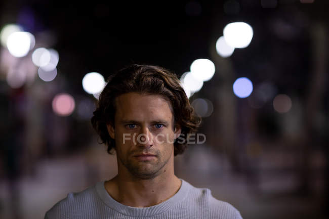 Porträt eines jungen kaukasischen Mannes auf der Straße, der abends direkt in die Kamera blickt — Stockfoto