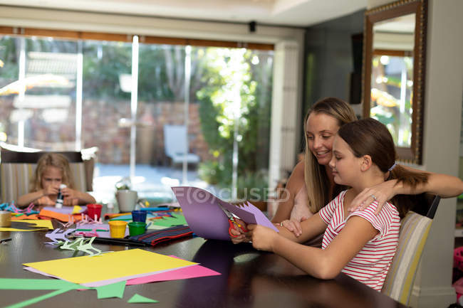 Side view of a young Caucasian woman doing crafts with her tween and younger daughters in their sitting — Stock Photo