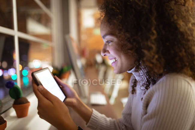 Side view close up of a smiling young mixed race woman standing and using a tablet computer in the office of a creative business — Stock Photo