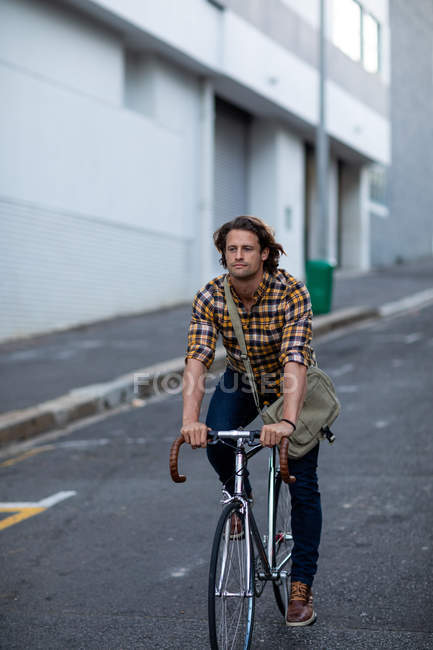 Vista frontal de un joven hombre caucásico en bicicleta, viajando a casa desde el trabajo por la noche - foto de stock