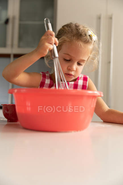 Вид спереди на молодую кавказскую девушку, смешивающую еду в миске для приготовления пищи на кухне — стоковое фото