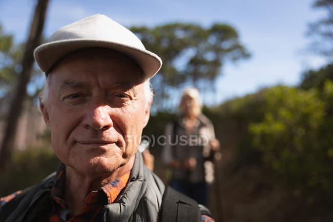 Retrato close up de um homem maduro caucasiano sorrindo para a câmera, com uma mulher caucasiana e campo atrás dele — Fotografia de Stock