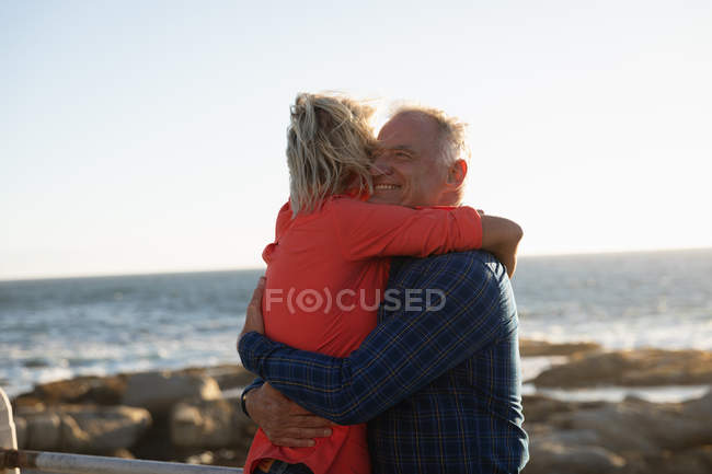 Вид збоку крупним планом посміхаючись зрілий Кавказький чоловік і жінка обіймаються під час прогулянки по морю — стокове фото