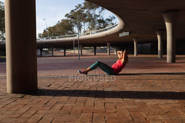 Side view of a young Caucasian woman wearing sports clothes doing crunches during a workout on a sunny day in a park — Stock Photo