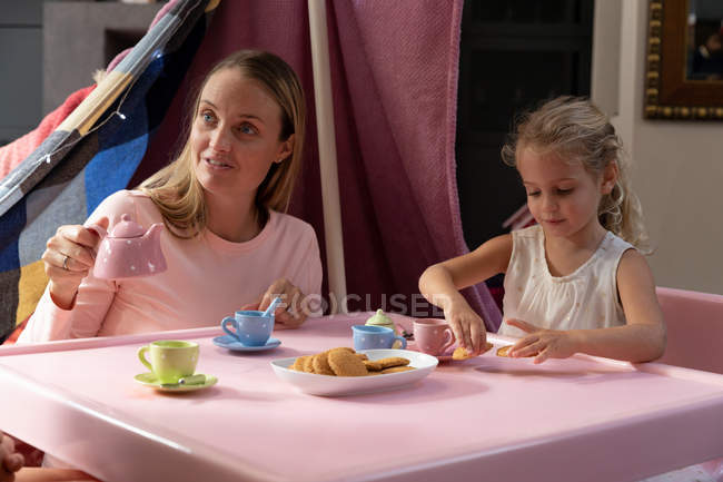 Vista frontal de uma jovem mulher caucasiana e sua filha fazendo uma festa de chá de bonecas em casa — Fotografia de Stock