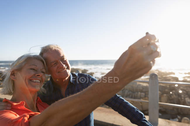Vista laterale da vicino di un uomo e una donna caucasici maturi che si fanno un selfie in riva al mare — Foto stock