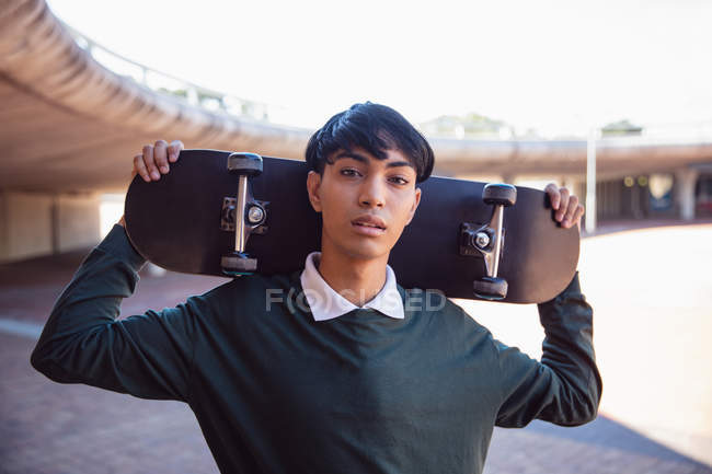 Porträt eines modischen jungen Transgender auf der Straße, der ein Skateboard in der Hand hält — Stockfoto