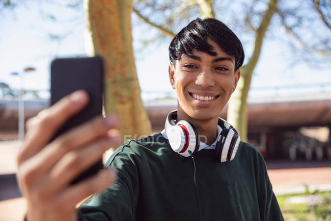 Front view of a fashionable young mixed race transgender adult in the street, taking a selfie with headphones on — Stock Photo