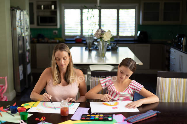 Front view of a young Caucasian woman doing crafts with her tween daughter in their sitting room — Stock Photo