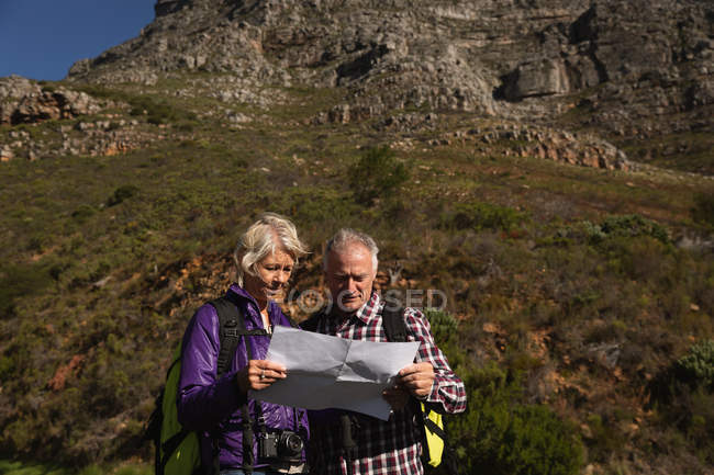Vista frontale da vicino di un uomo e una donna caucasici maturi che leggono una mappa durante una passeggiata in un ambiente rurale, con le montagne sullo sfondo — Foto stock