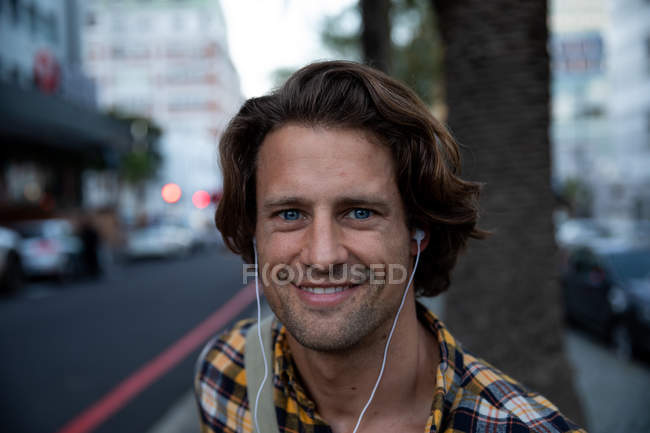 Портрет молодого кавказца на улице с наушниками на улыбке перед камерой вечером — стоковое фото