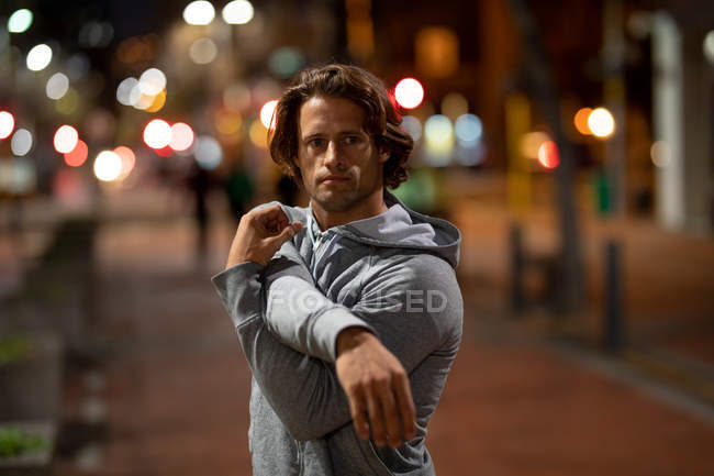Retrato de un joven caucásico que se extiende en la calle durante su entrenamiento nocturno - foto de stock