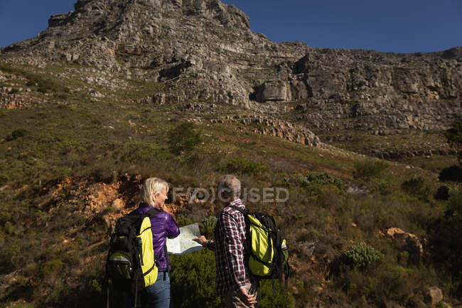 Vista trasera de cerca de un hombre y una mujer caucásicos maduros leyendo un mapa durante un paseo en un entorno rural, con montañas en el fondo - foto de stock