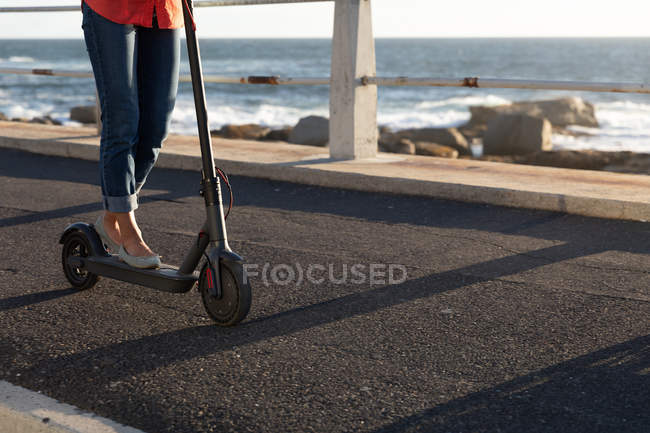 Nahaufnahme einer Frau mit einem E-Roller am Meer bei Sonnenuntergang — Stockfoto