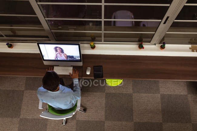 Над головою дивиться на молодого кавказського чоловіка, який працює в офісі творчого підприємства сидячи за столом за вікном, користуючись комп 