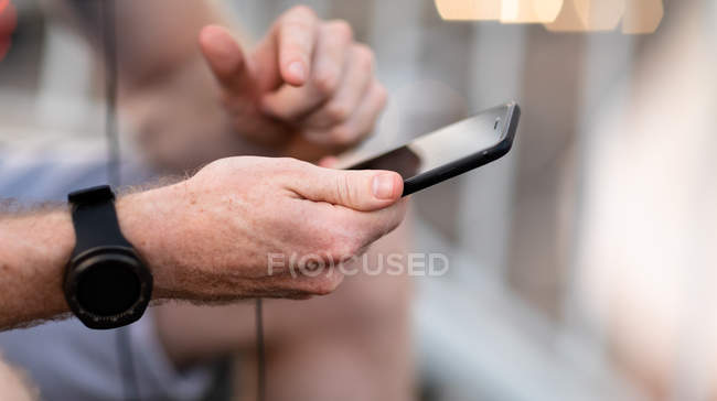 Close up of hands of man exercising on a footbridge in a city, sitting on steps and using a smartphone during a break — Stock Photo