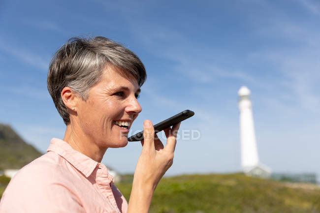 Front view of an middle-aged adult caucasian woman couple enjoying free time relaxing on a sunny beach near a light house beside the sea — Stock Photo