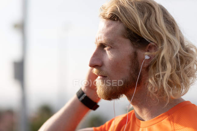 Side view close up of a young athletic Caucasian man exercising on a footbridge in a city, listening to music with earphones on — Stock Photo