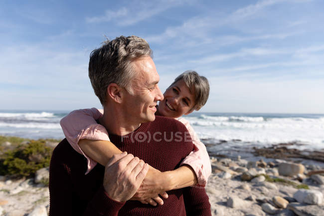 Vista frontal close-up de um casal adulto caucasiano desfrutando de tempo livre abraçando juntos em uma praia ao lado do mar em um dia ensolarado — Fotografia de Stock