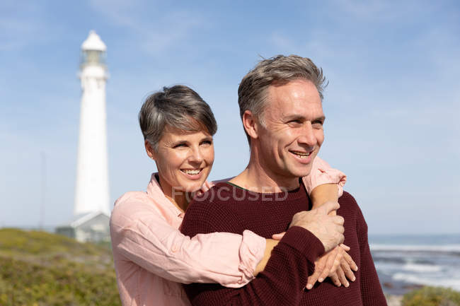 Vue de face gros plan d'un couple adulte caucasien jouissant de temps libre embrassant ensemble au bord de la mer par une journée ensoleillée — Photo de stock