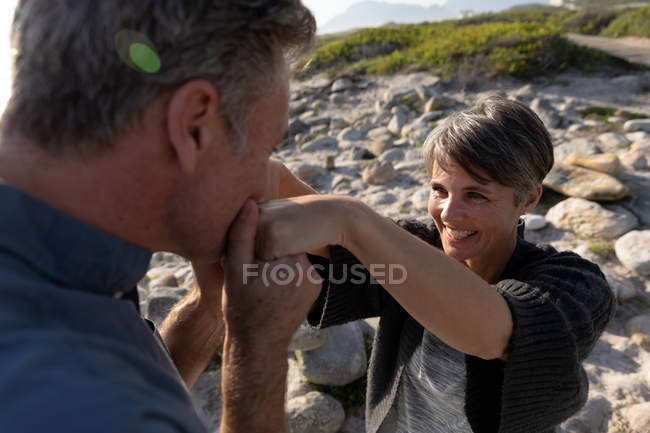 У сонячний день перед очима доросла кавказька пара проводить вільний час, цілуючи руки на пляжі. — стокове фото