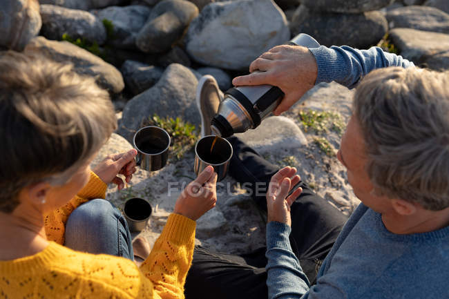 Vista aérea de cerca de una pareja caucásica adulta disfrutando de tiempo libre relajándose juntos tomando café en un día soleado - foto de stock
