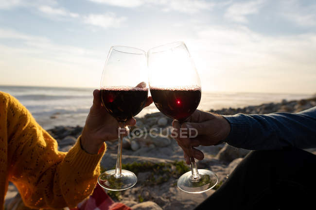 Руки пари насолоджуються вільним часом, розслабляючись разом на пляжі біля моря, п'ють вино в сонячний день — стокове фото