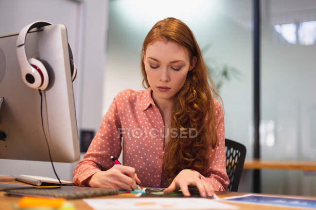 Передній погляд на молоду кавказьку жінку, що працює в творчому кабінеті, пише і сидить за столом з комп'ютером на — стокове фото