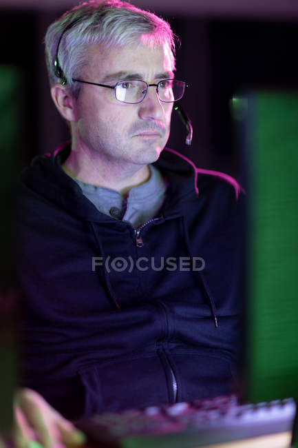 Передній погляд на кавказького чоловіка, який працює в творчому офісі, з окулярами для читання та навушниками, дивлячись на екран комп 